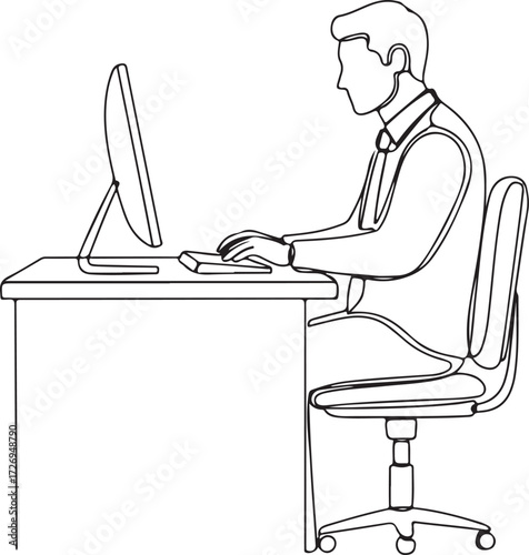 A woman is sitting at a desk working on her laptop while reading a book or newspaper near a kitchen