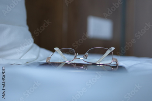 Glasses on bed Stylish lamp, book and glasses on bedside table indoors. Bedroom interior elements