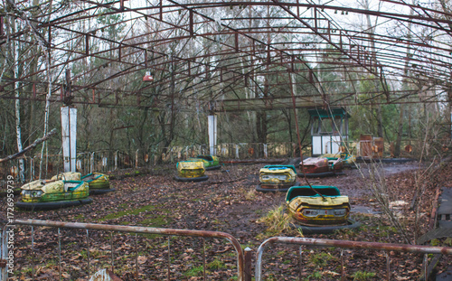 Fotografie Eerie Chernobyl scene of rusty, abandoned bumper cars overrun by nature, casting a haunting, desolate vibe