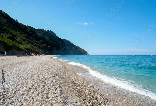 Sunny day at the pebbles beach across the cliffs in Marche, Italy.  Coastline, horizontal line, natural background. turquoise water