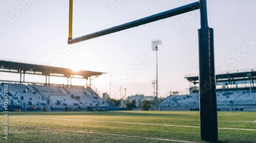 Football goalpost on empty stadium field under dramatic sunset lighting.