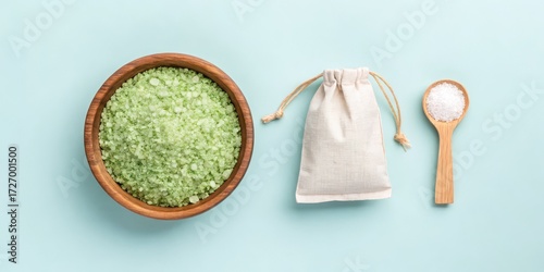 Green bath salts in wooden bowl with bag and white salt on wooden spoon on blue background
