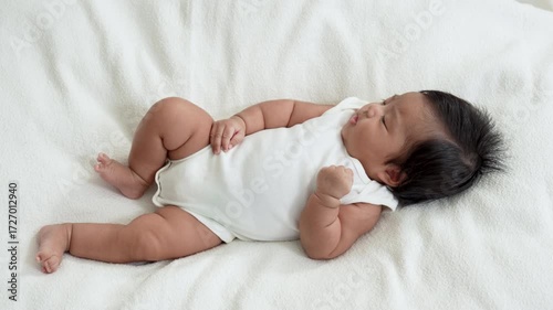Asian newborn baby girls wearing a white bodysuit laying on the bed.
