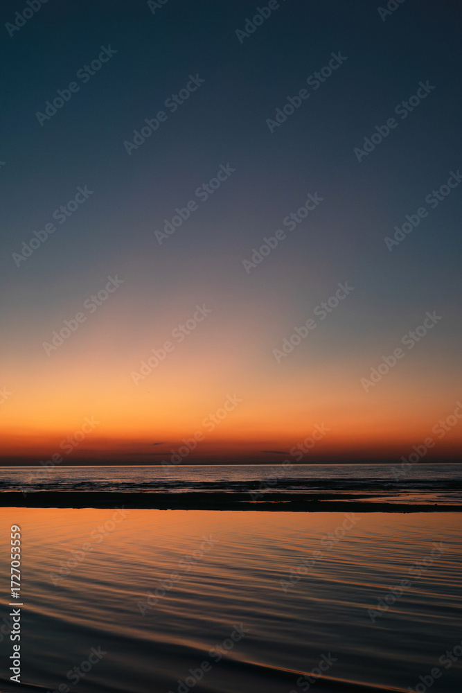 Fototapeta premium Tranquil seascape at sunset with vivid orange and blue gradient sky reflecting on calm ocean waves