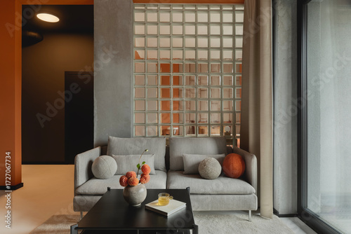 Obraz na płótnie Stylish living room with gray sofa, textured wall, glass block partition and warm-toned accessories