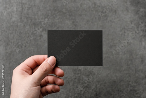 Hand holding blank black business card on textured gray background
