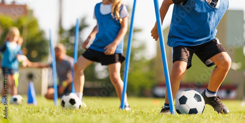 School boy dribbling soccer ball in slalom training drill. Football training camp for school kids. Soccer practice equipment on grass pitch