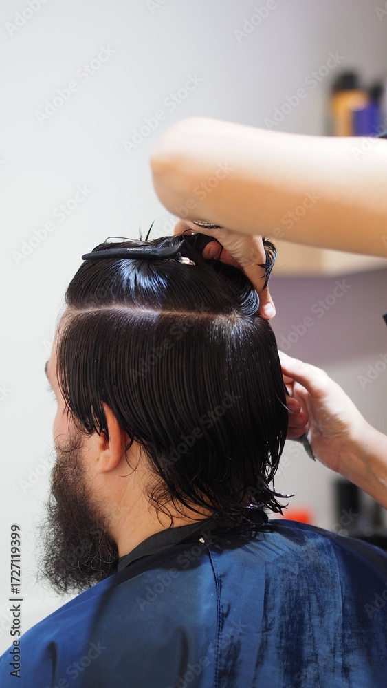 Fototapeta premium Hairstylist attaching a new capillary prosthesis to a man's head sitting on a salon