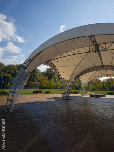 Fotografi Modern outdoor pavilion with a curved canopy structure, surrounded by lush green