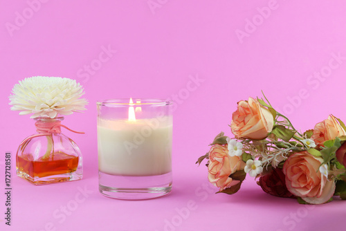 burning luxury aromatic scented candle glass is on pink table with aroma reed diffuser and background of pink wall of house in bed room to create relax and romantic moment for lovers on Valentine day