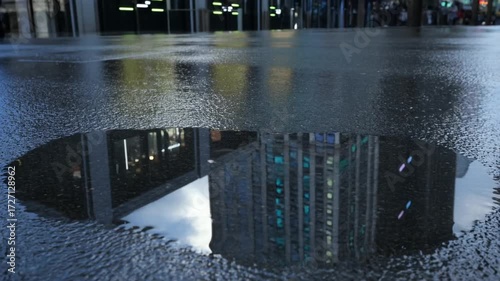 Skyscraper reflection in urban puddle on textured wet pavement
