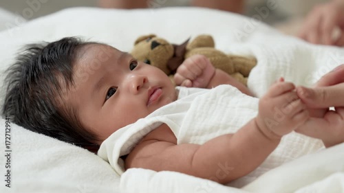 Asian newborn baby girls wearing a white bodysuit laying on the bed.