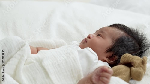 Asian newborn baby girls wearing a white bodysuit laying on the bed.