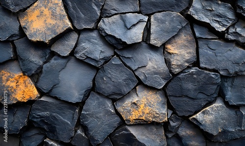 A close up shot of a wall made of dark gray and black rocks with some yellow and brown discoloration