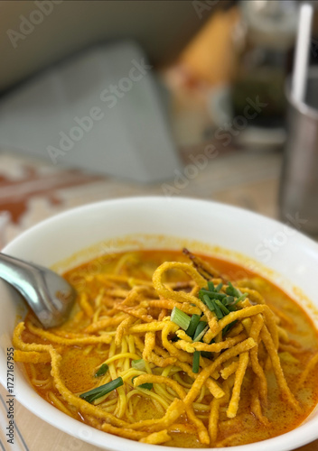Delicious Northern Thai Curry Noodle Soup with Crispy Fried Noodles and Fresh Herbs in a White Bowl