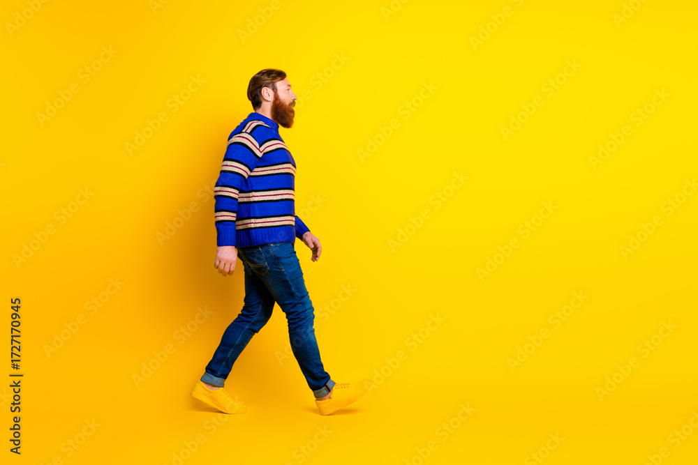 Naklejka premium Young man with red hair and beard walking in a yellow background wearing a stylish striped sweater and casual jeans