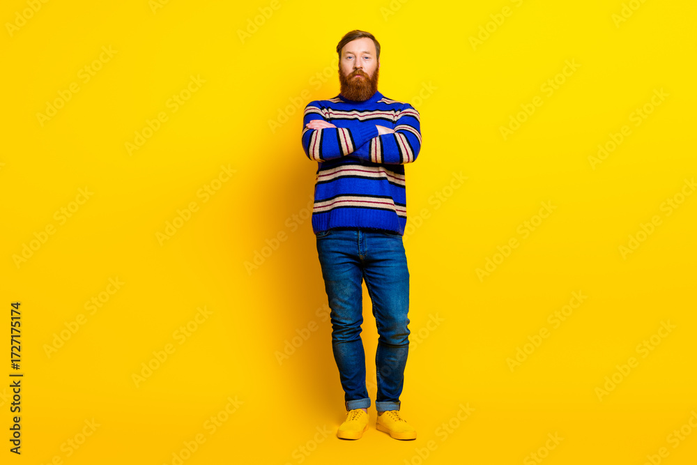 Fototapeta premium Fashionable bearded man in striped sweater poses against a vibrant yellow background, showcasing casual modern style