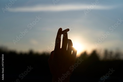 Hand holding a half-smoked cigarette against the backdrop of a sunset sky.