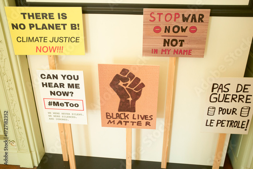Protest signs demand climate action, equality, peace, and justice on wooden sticks indoors. Brussels, Belgium