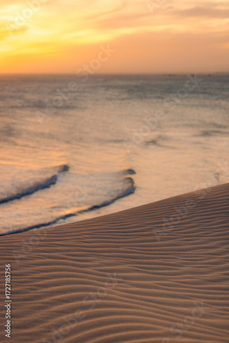 Golden sunset over rippled sand dunes leading to a calm ocean with gentle waves. Ke Ga, Binh Thuan, Indonesia