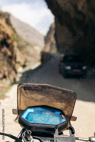A dusty mountain road enters a shaded cliff tunnel with a motorbike dashboard in the foreground. Road F042 of Annapurna in Mustang District of the Gandaki Province, Nepal