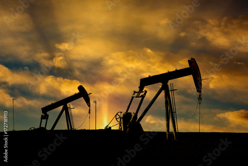 Silhouetted oil pumps against a dramatic, golden sunset sky. Alberta, Canada