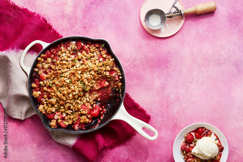 Strawberry crumble with ice cream on a pink background and a scoop nearby.