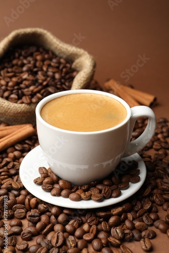 Cup of hot coffee, beans and cinnamon on brown background, closeup
