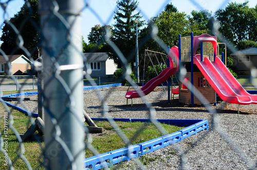 View of a fenced playground behind a chain-link fence with homes in the background
