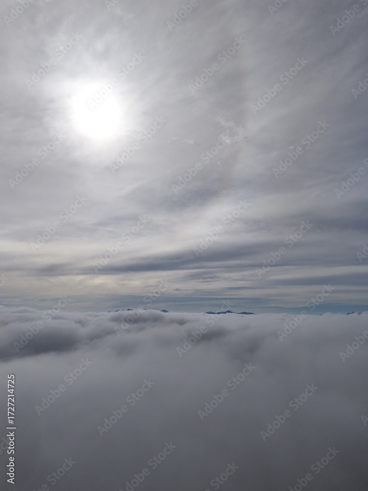 Obraz premium Serene aerial skyscape. Drone image at dawn above the clouds. Aerial view above a dense sea of clouds, with soft sunlight and a subtle halo in the sky.