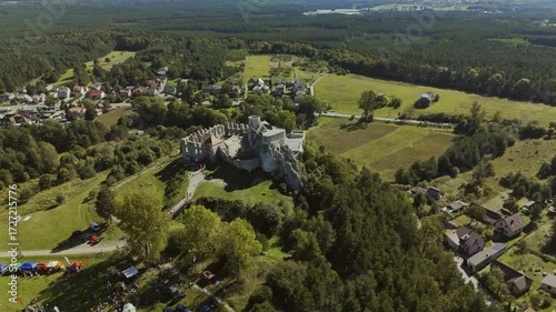 Aerial drone footage circling Rabsztyn Castle in Poland during summer, showcasing the medieval fortress, stone walls, and surrounding lush greenery from all angles.
