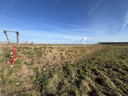Red post with a barricade tape with an RWE lignite excavator in the Hambach open-pit mine, as well as power plant cooling towers in the background near the village of Bürgewald (formerly Morschenich),