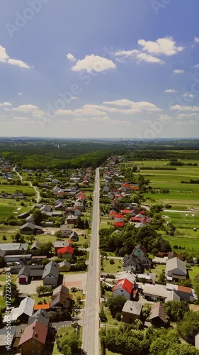 A cinematic drone tilt shot of Suloszowa village in Poland, revealing its long main street and surrounding colorful fields that create a unique rural landscape.