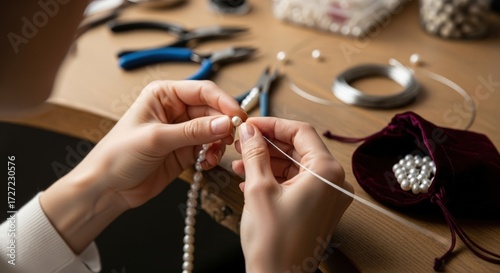 Close-up of hands threading pearls onto a string on a workbench with jewelry-making tools.