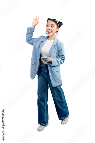Full body Asian Woman cheerfully waving while holding a phone. She wears a blue blazer and jeans, exuding modern charm on PNG
