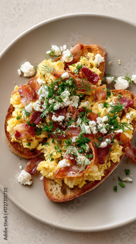 Scrambled eggs topped with crispy bacon and fresh herbs served on toasted bread on a neutral plate