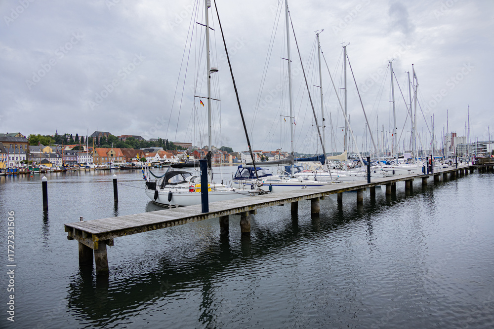Fototapeta premium Wooden pier with moored yachts and colorful waterfront houses in Flensburg harbor