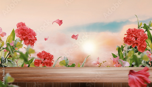 Empty wooden table top with blurred beautiful sunset and clouds background, surrounded by hibiscus flowers and other plants. Scenic summer evening banner with copy space. 