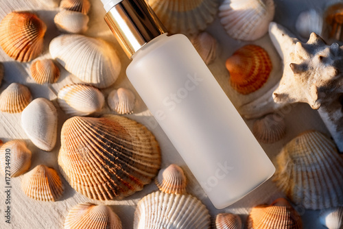 A frosted glass cosmetic bottle with a gold pump lies among various seashells on a sunlit surface, evoking luxury skincare and a fresh beach-inspired atmosphere
