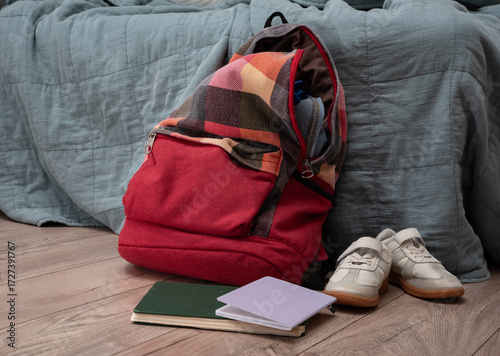 Konstfotografi pair of children's sneakers, scattered books and a red checkered colorful backpack lie on the floor in the room