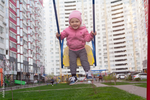 Cute baby on the swing on the playground near the house