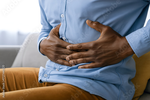 Man Clutching Stomach with Abdominal Pain Sitting in Distress Indicating Gastrointestinal Discomfort