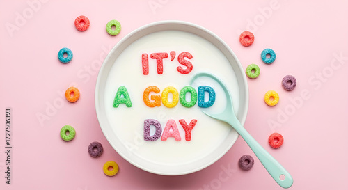 Inspirational message 'It's a Good Day' spelled out with colorful alphabet cereal in a bowl of milk, viewed from above on a pink background