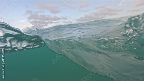 Camera captures half above and half below sea level with visible foam, bubbles and moving waves in slow motion.