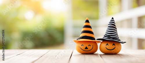 Happy Halloween pumpkins with cute smiling faces and striped witch hats on wooden table.