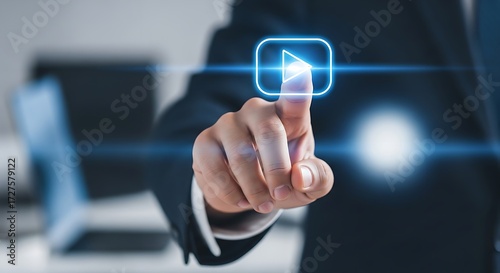 A hand pressing a glowing blue play button in a digital interface with a suit and laptop behind it