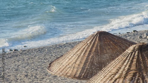 A windy day on a tranquil beach. Gentle waves roll onto the shore as a brisk breeze rustles the tops of the thatched umbrellas.Seagull flies over a windy beach.
