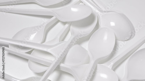 Disposable plastic spoon on rotating white background. Concept of global environmental problems, waste reduction, recycling of non-biodegradable trash, overconsumption, carbon footprint. 