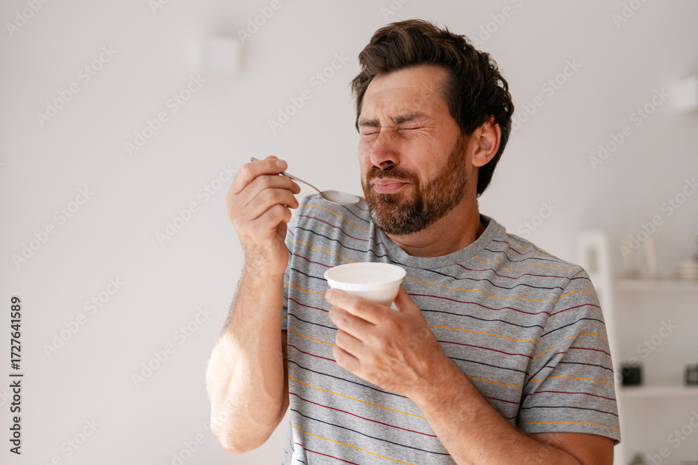 Fototapeta premium Middle aged, bearded man reacting with disgust while eating unpleasant yogurt