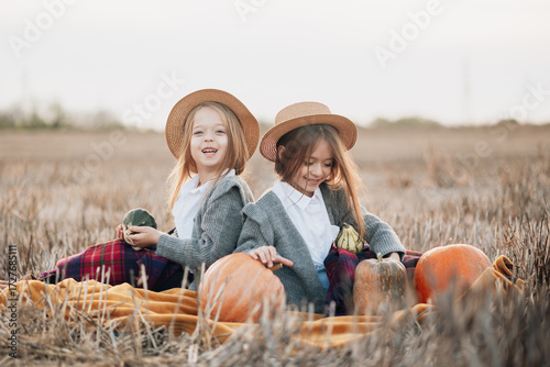 Two children enjoy an autumn day picking pumpkins in a cozy field while dressed in warm clothes and straw hats